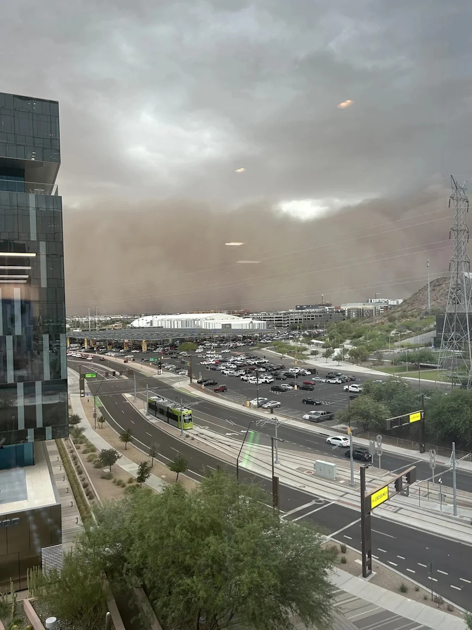 Dust storm approaching a city with roads, traffic, and buildings visible. Sky is overcast