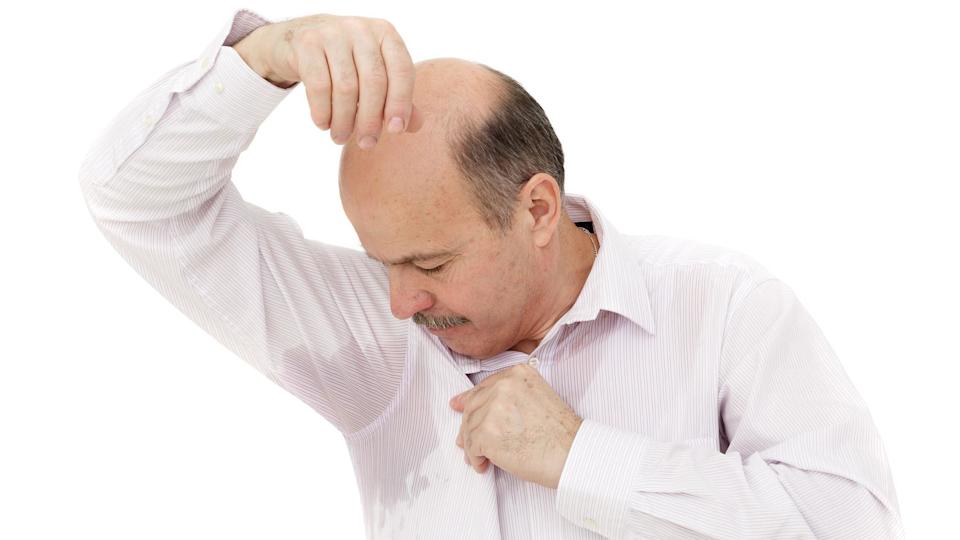 Un hombre observa su camisa manchada por la transpiración de su axila.