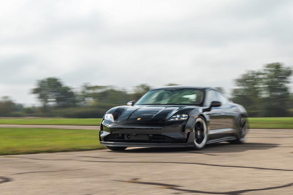 front view of a black porsche taycan turbo gt in motion on a track, highlighting its aerodynamic design and led headlights.