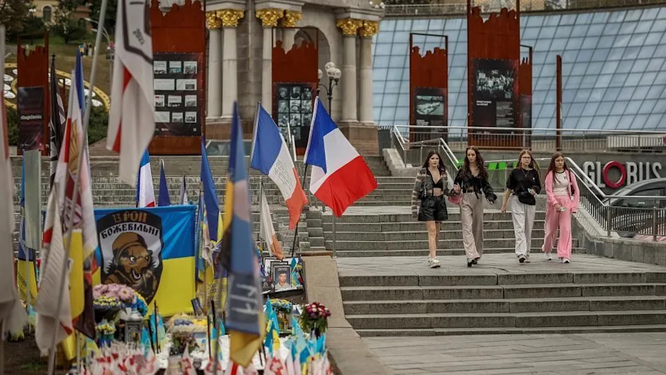 People pass by a makeshift memorial to fallen Ukrainian defenders in Kyiv's Independence Square. Along with flowers and the Ukrainian flag there are also flags of other countries, including France.