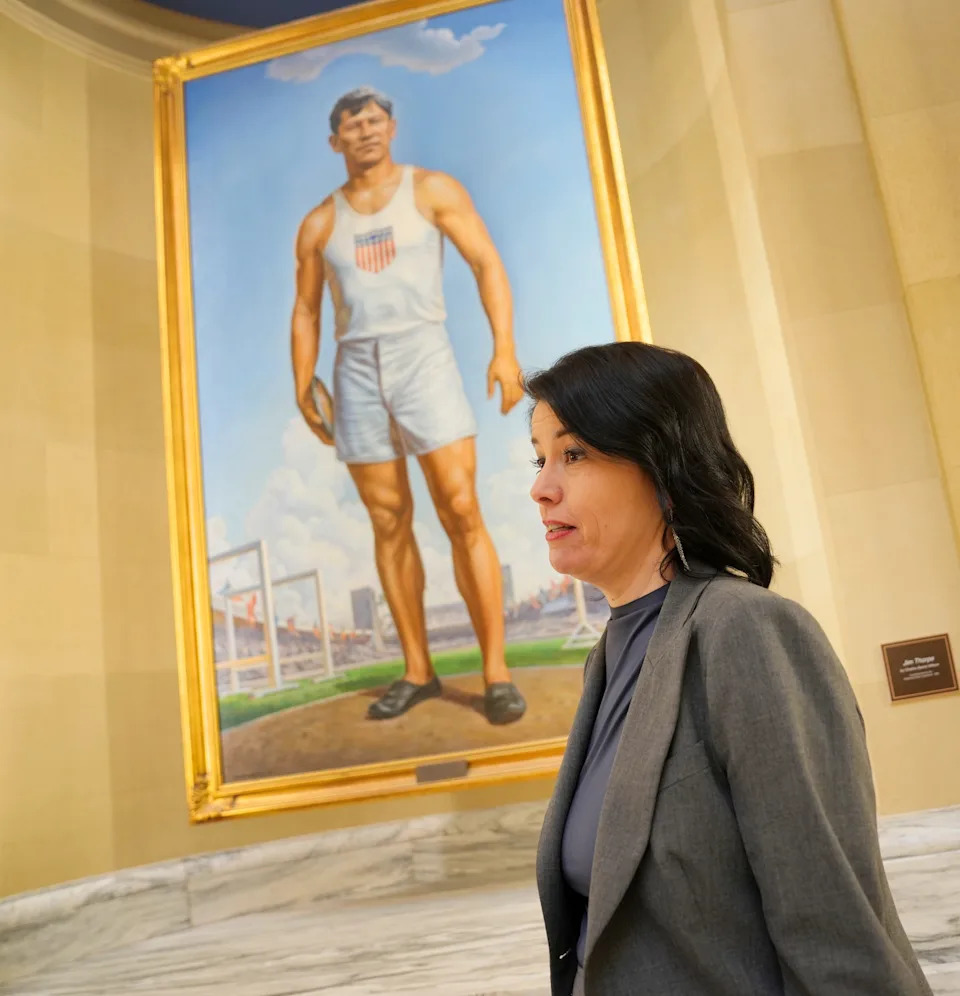 Amber Sharples, with the Oklahoma Arts Council, stands in front of the painting of Jim Thorpe by Charles Banks Wilson in March on the fourth floor of the state Capitol. The Oklahoma Arts Council is taking cost-cutting measures, including suspending its program of rotating exhibitions in the Oklahoma State Capitol galleries.