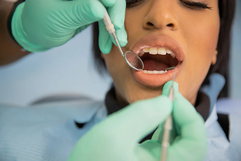 A person at the dentist's office, receiving a dental examination with tools in their mouth