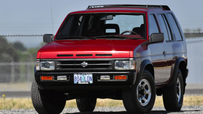 A red 1993 Nissan Pathfinder parked in front of a chainlink fence