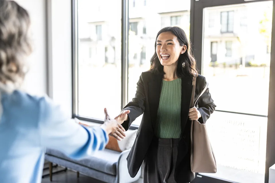 Person in business attire greets someone with a handshake in a bright office setting