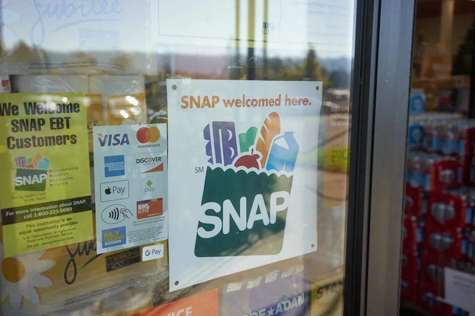 Store window displays SNAP acceptance signs and various payment method stickers