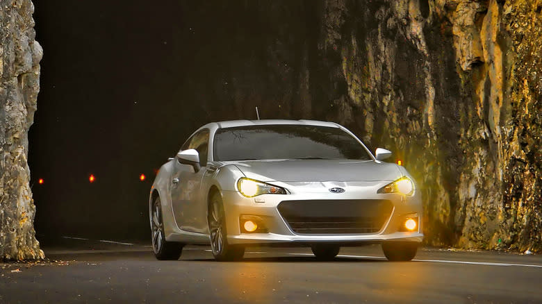 A silver Subaru BRZ driving out of a tunnel carved into a mountain