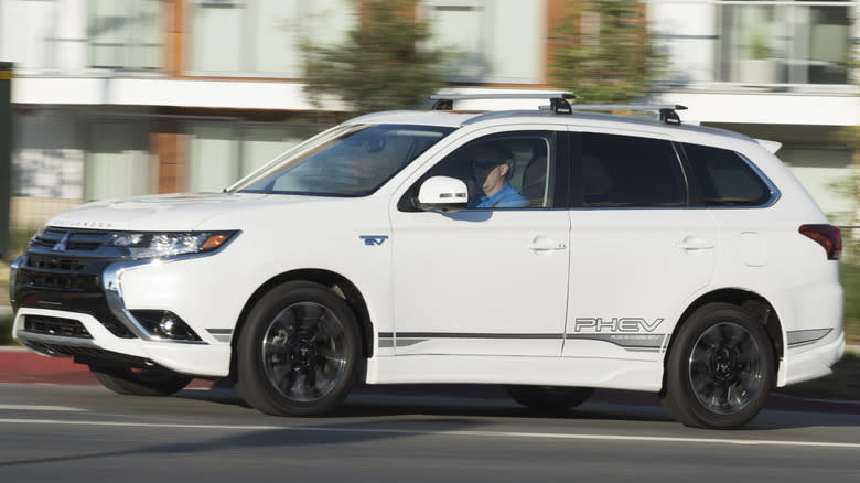 A white Mitsubishi Outlander PHEV driving past a building