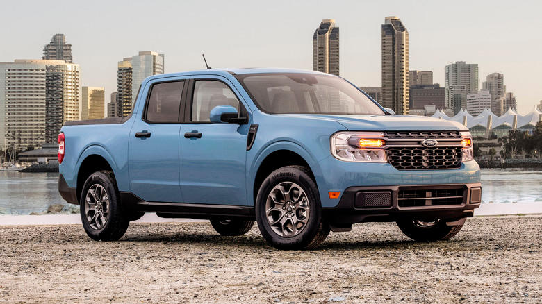 2022 Ford Maverick Hybrid XLT parked on a dirt surface with a body of water and city skyline in the background