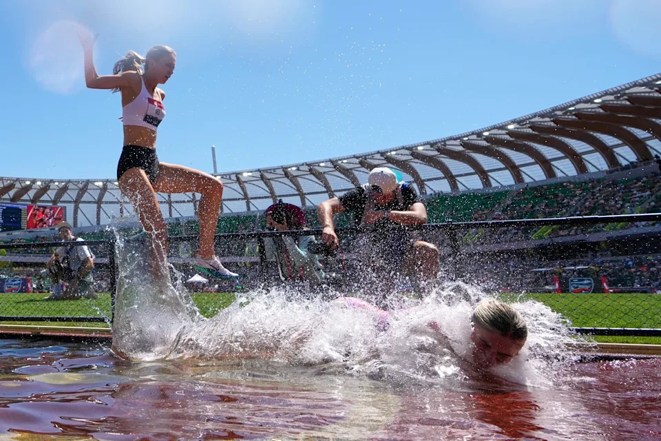 A runner stumbles and falls into a water obstacle during a race.