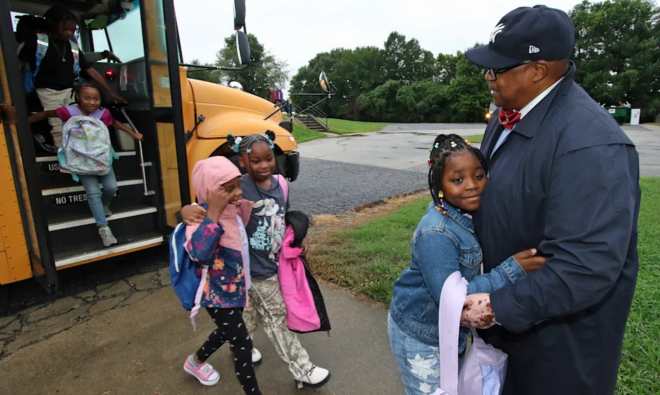 Terry Barnwell greets students as they get off the bus for the first day of school early Wednesday morning, Aug. 13, 2025, at Woodhill Elementary School in Gastonia.