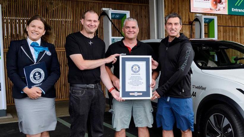 A Guinness world record adjudicator alongside three men holding a framed certificate next to a white Polestar 3 SUV. 