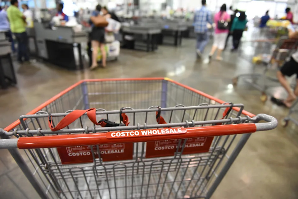 A shopping cart inside a busy Costco store with people checking out in the background