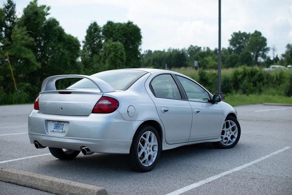 rear three quarter view of silver sedan with spoiler parked in lot near trees.