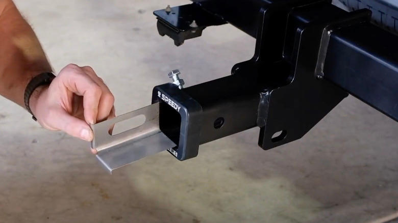 A person installing a metal shim in a trailer hitch receiver