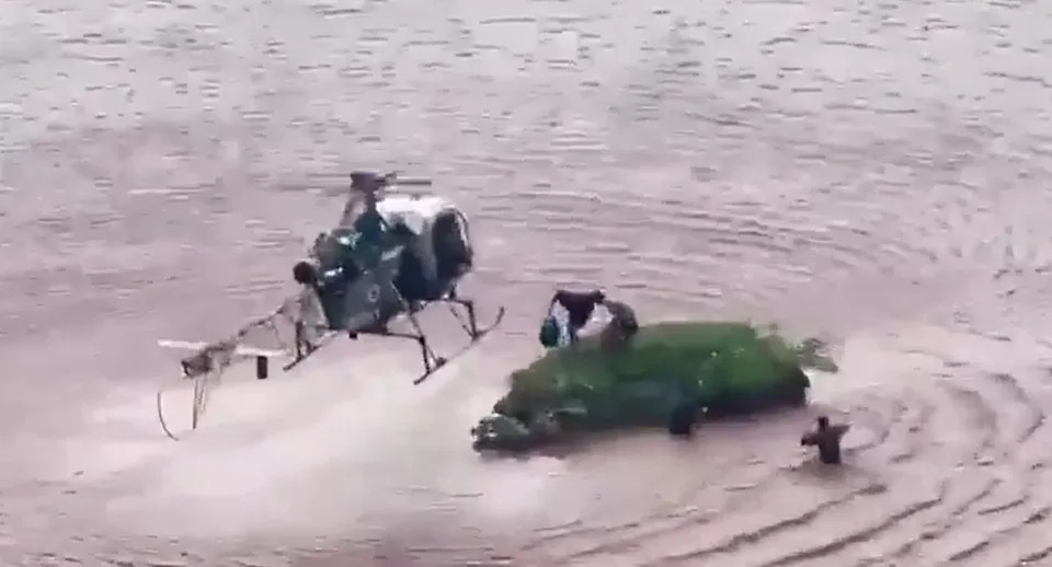 The indian Army helicopter picks up two people needing rescue from a grassy patch above flooding.