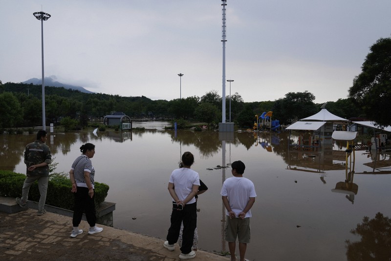大雨で水浸しになった公園を眺める人たち＝北京市密雲区で2025年7月28日、AP