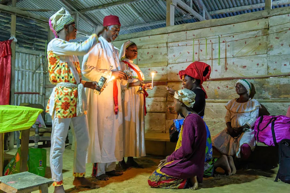 Several people wearing headdresses and long robes appear to be blessing others, while some are kneeling before them.