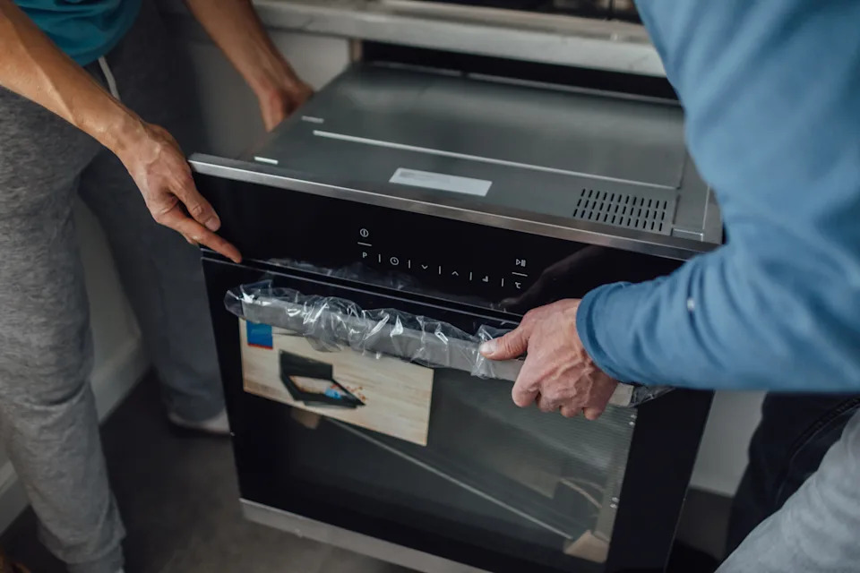 Two people installing a built-in oven in a kitchen, focusing on teamwork and home improvement tasks