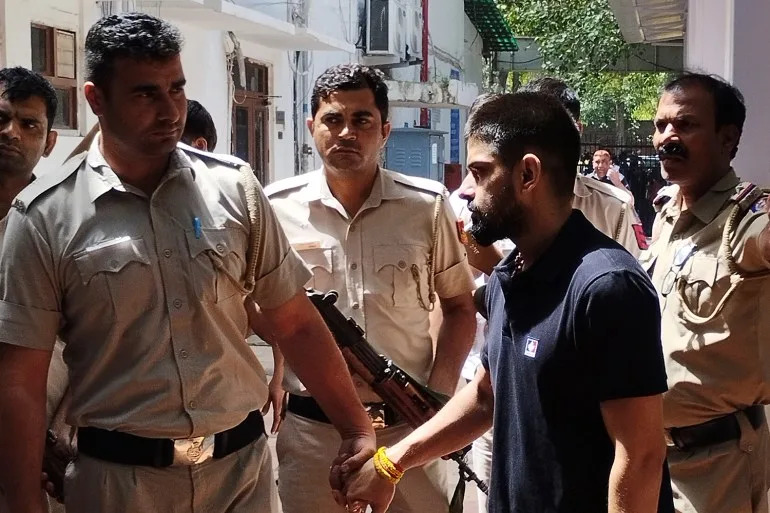 Policemen escort jailed gangster Lawrence Bishnoi as they bring him to produce before the Patiala House court in New Delhi, India, Tuesday, April 18, 2023. (AP Photo/Dinesh Joshi)