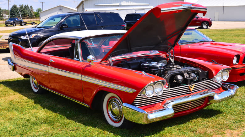 A red "Christine" 1958 Plymouth Fury with a 350 Golden Commando V8 sits on grass at a car show