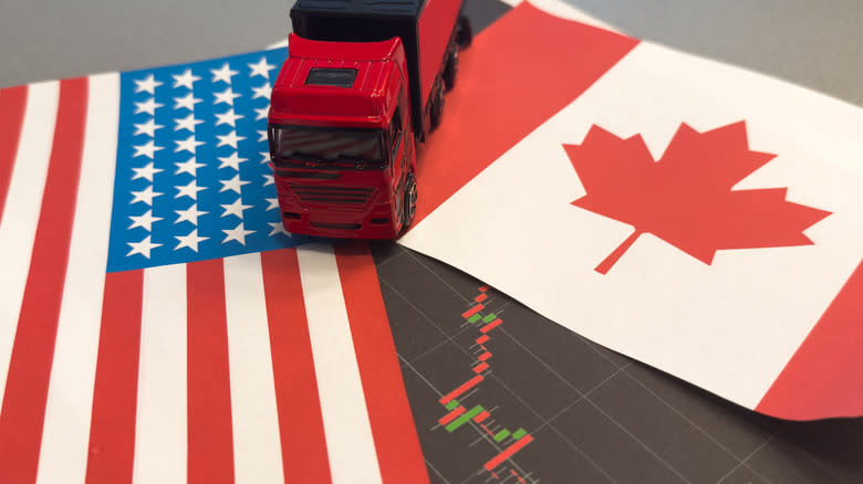 a truck sits between a u.s. flag and canadian flag on a picture of falling stock prices