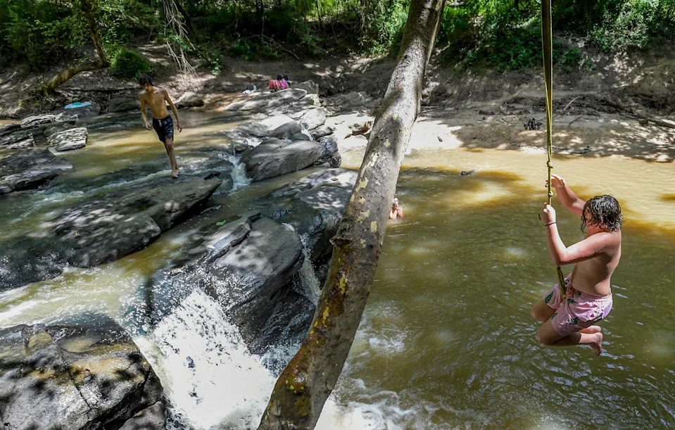 Chris Emfinger swings over Corn Creek while cooling off in Wetumpka, Ala., on Wednesday July 10, 2024.