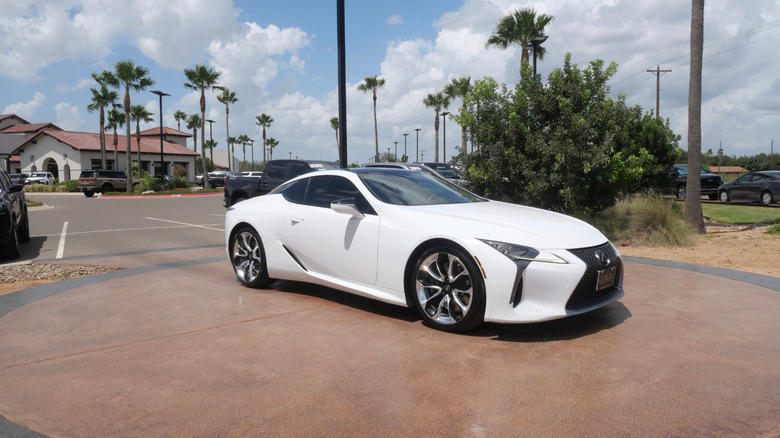 a white Lexus LC500 parked outside on a sunny day, with palm trees and a old mission style building in the background