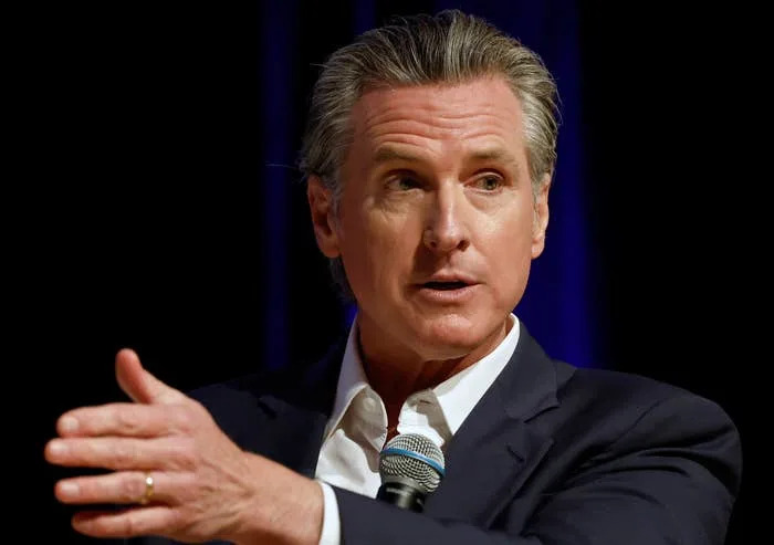 Person in a suit speaking into a microphone, gesturing with one hand
