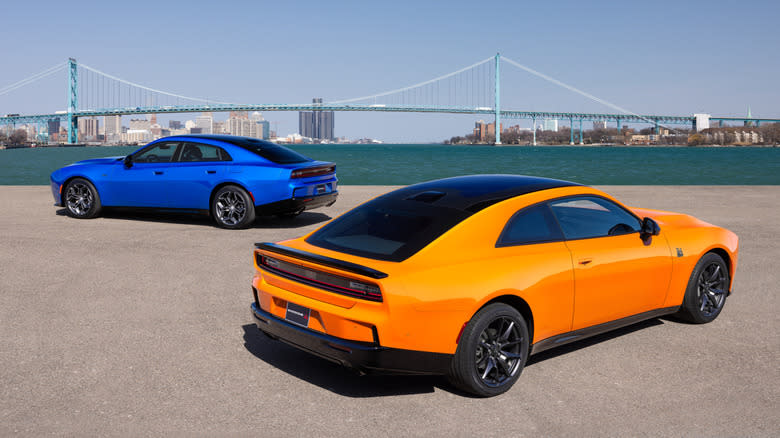 Rear 3/4 view of an orange 2026 Dodge Charger coupe and a blue Charger sedan