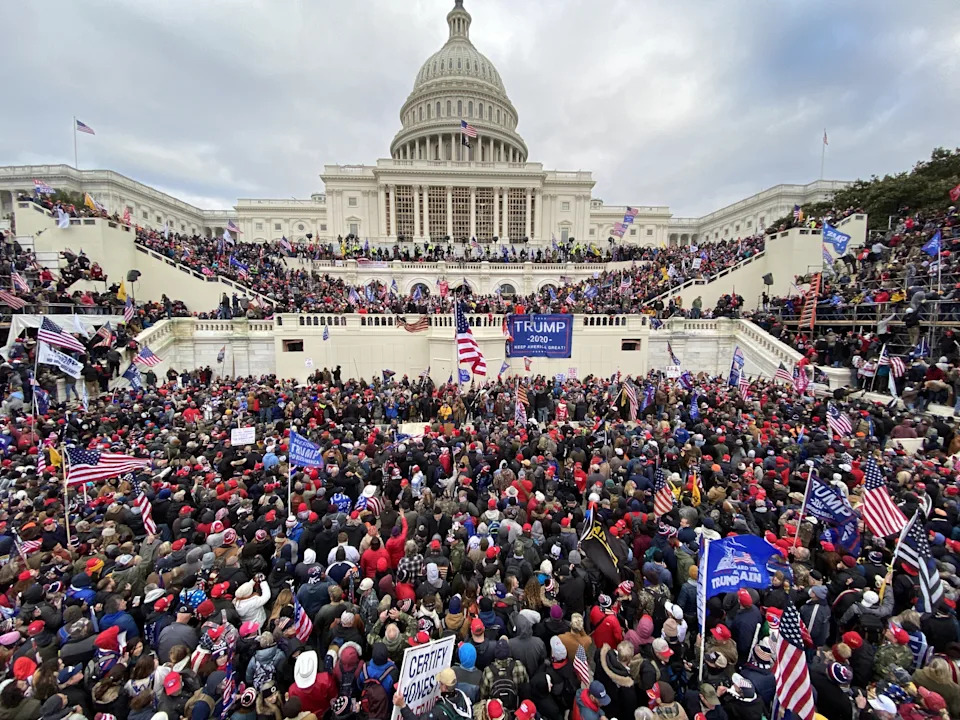 Large crowd gathered outside the U.S. Capitol building, many holding American flags and banners, during a significant public event