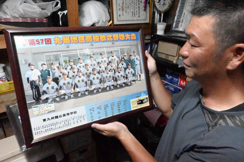 久保田愛悠さんが出場した大会の集合写真を見つめる東九州龍谷軟式野球部の陣野雅紀監督＝大分県中津市で2025年8月20日午後7時2分、山口泰輝撮影