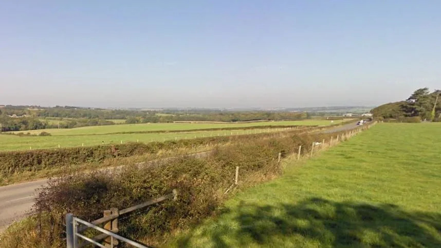 A Google Street View of Briddlesford Road, a country road that lies between fields.