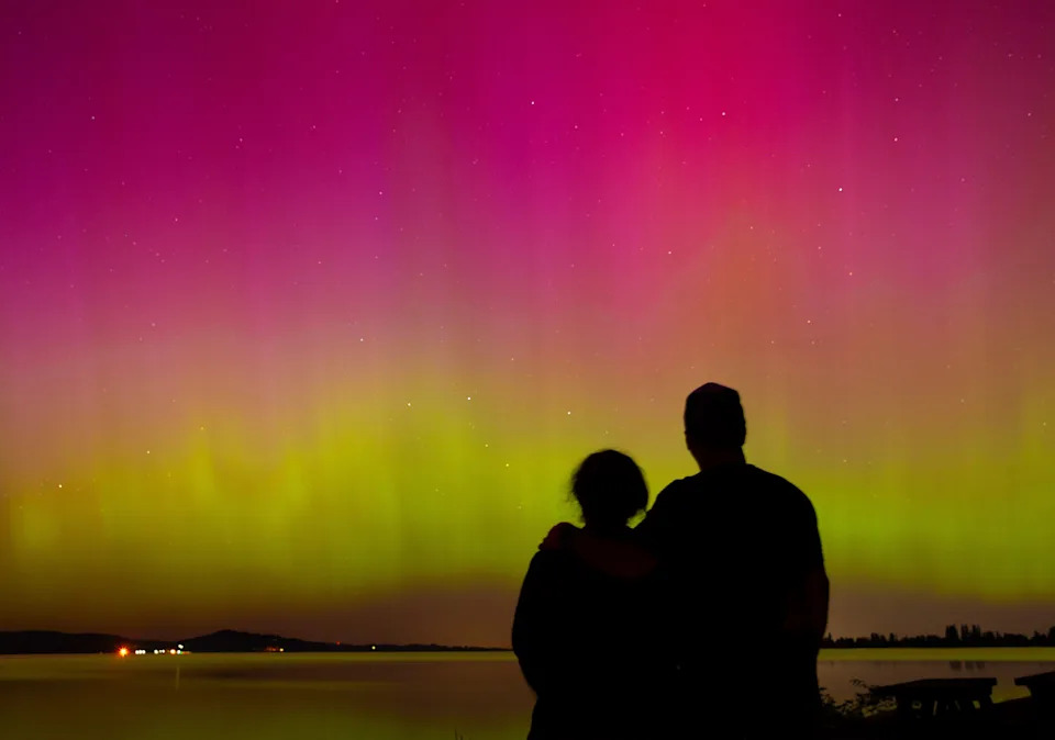 A couple watches the northern lights from Perkins Peninsula Park on the shores of Fern Ridge reservoir west of Eugene, Oregon on May 10, 2024