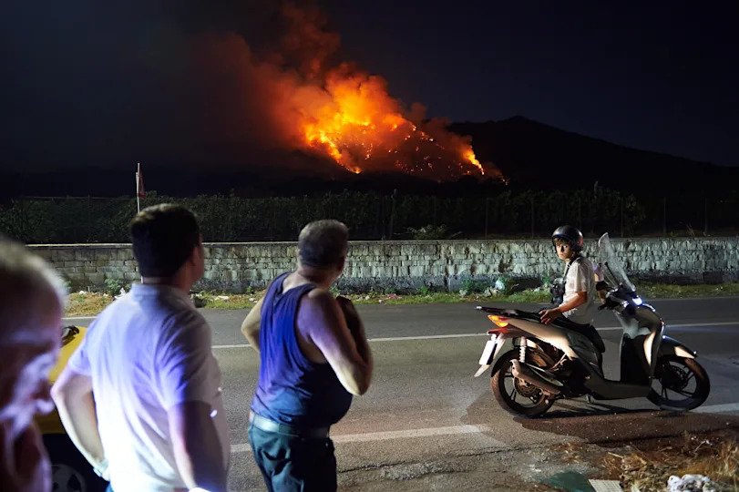 People watch the flames and smoke rising from a wildfire that breaks out at the Vesuvius National Park in Terzigno, a commune in Naples, Italy on August 8, 2025. / Credit: Eliano Imperato/Anadolu via Getty Images