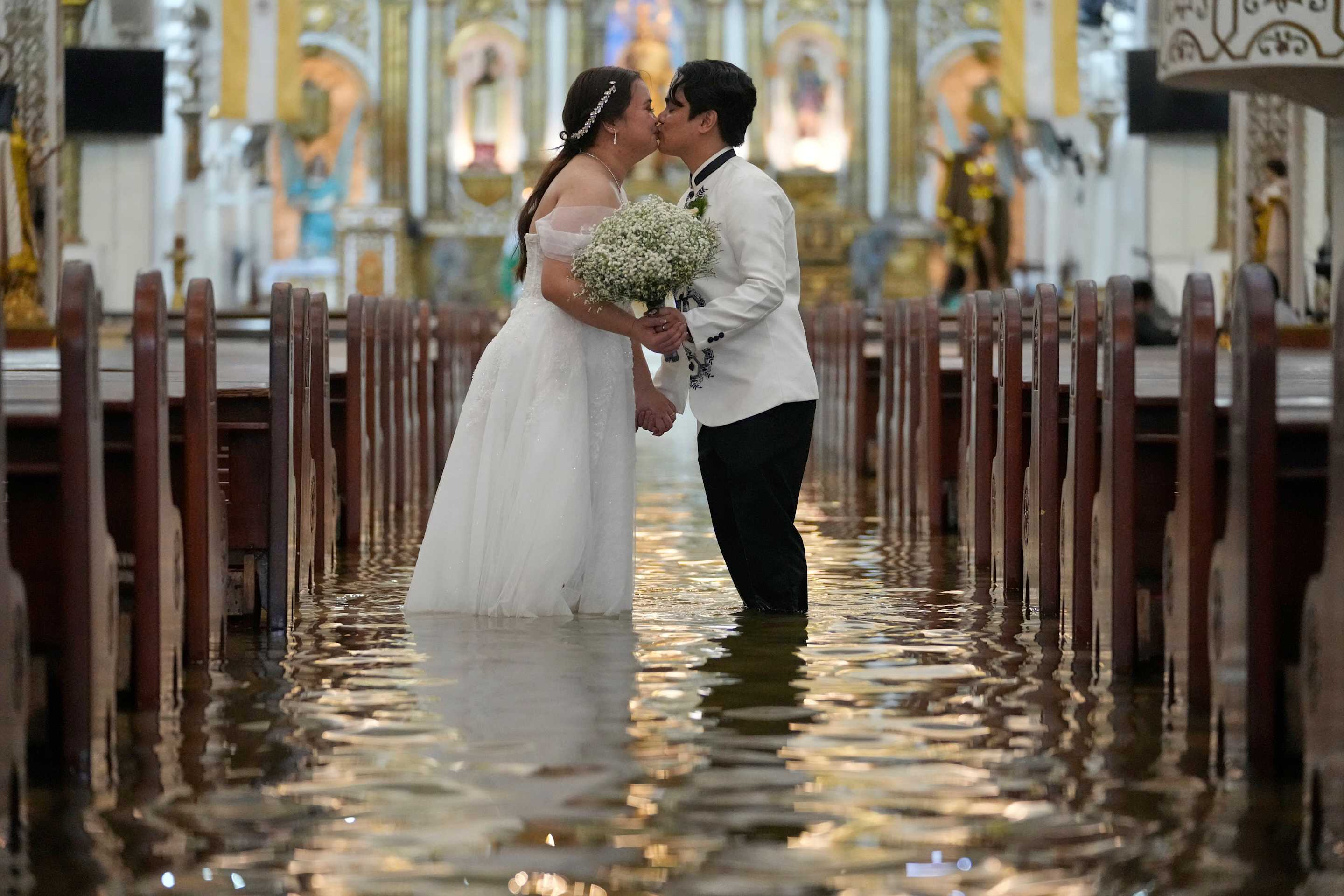 Los recién casados Jade Rick Verdillo (derecha) y Jamaica Aguilar se besan durante su boda en la inundada iglesia de Barasoain, en Malolos, capital de la provincia de Bulacán, Filipinas, el martes 22 de julio de 2025. (AP Foto/Aaron Favila)