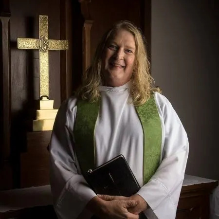 Gwen Fry poses for a photo in front of a cross that is affixed to a wall. 