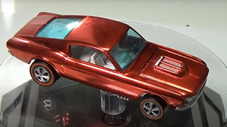 A restored strawberry over chrome 1968 Ford Mustang on a display stand.