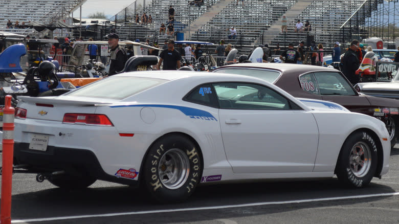A white Chevrolet COPO Camaro at a car even with bleachers in the background