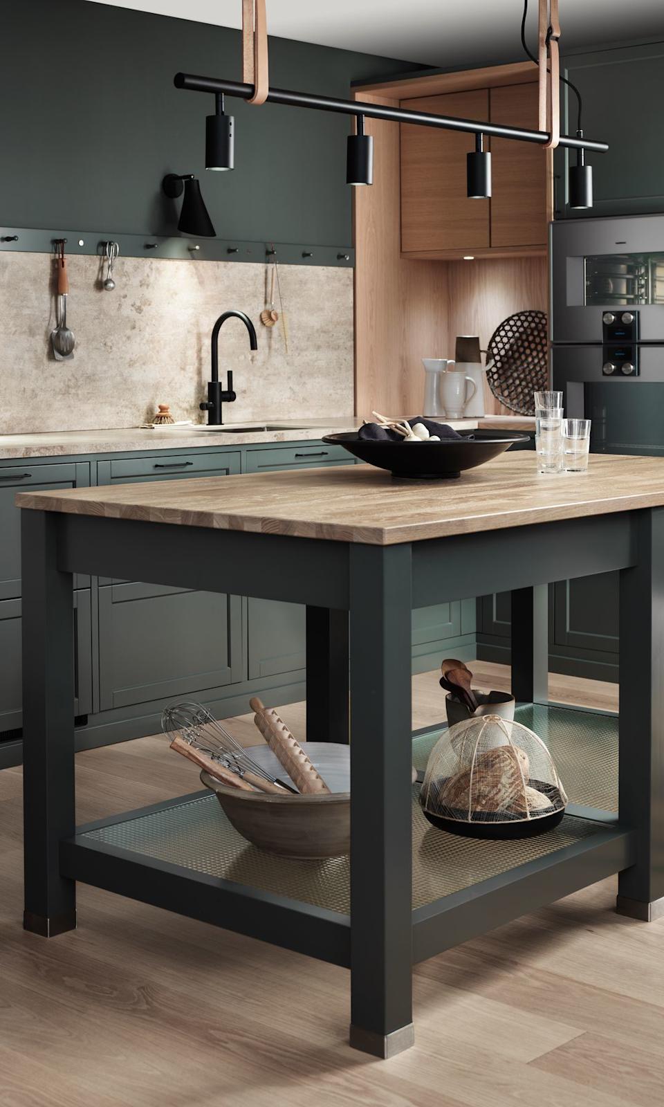 Cocina con mesa de trabajo a modo de isla, en color verde oscuro con sobre de madera y balda inferior