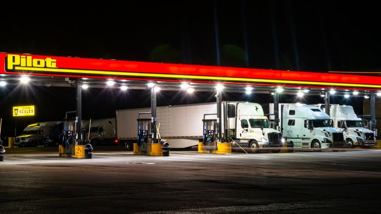 A Pilot truck stop at night, with three semi trucks in gasoline bays