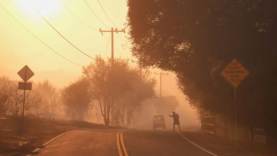 A person walks toward a vehicle with wildfire smoke filling the air