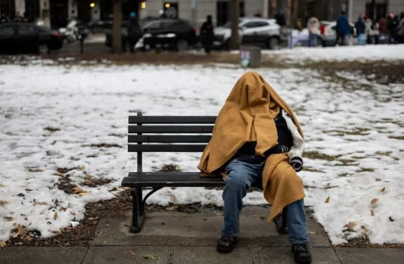 A homeless person sits on a bench in a park, ahead of the presidential inauguration of U.S. President-elect Donald Trump, in Washington, U.S., January 18, 2025. (credit: REUTERS/Marko Djurica/File Photo Preview)