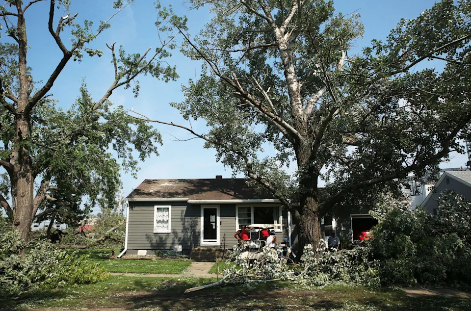 Hudson residents gather under a patch of shade Tuesday, July 29, 2025 as they take a break from cleaning up debris after severe weather moved through the area Monday evening damaging trees, homes and other structures. (Makenzie Huber/South Dakota Searchlight)