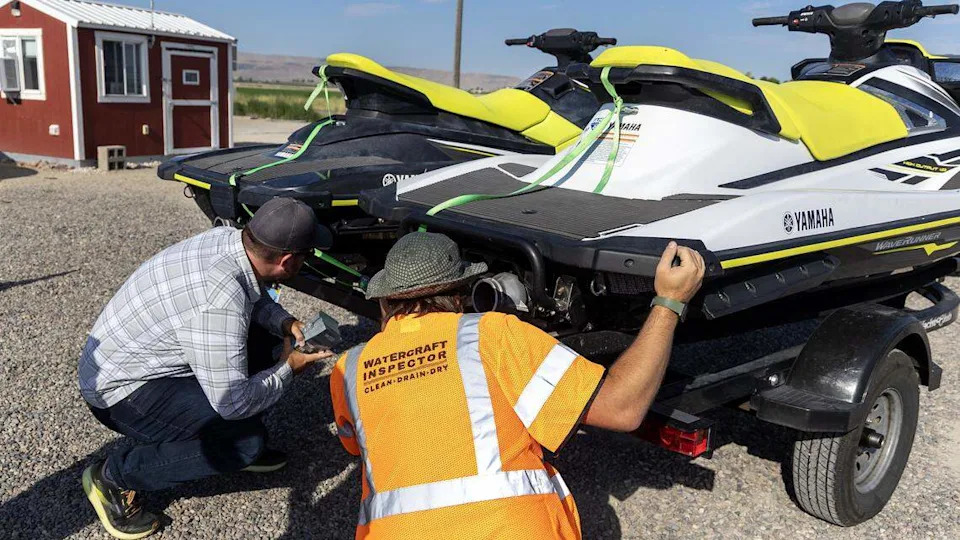 Watercraft inspector Mark Klug, right, looks at drain plugs on two jet skis last used in Nevada at a watercraft boat inspection station in Marsing, July 25, 2025.