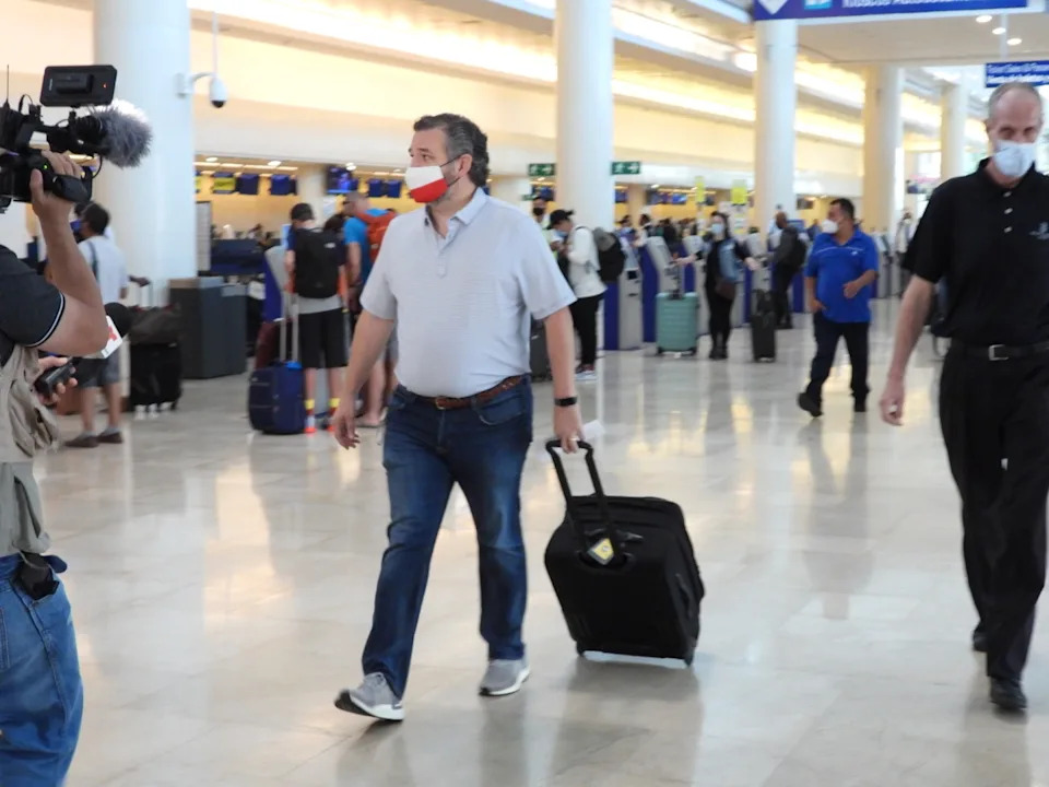 Person with a suitcase walking through an airport, filmed by a camera crew. Passengers are in the background