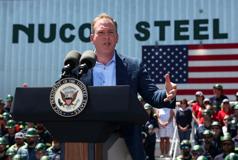 EPA administrator Lee Zeldin stands in front of a Nucor Steel building with an American flag in the background.