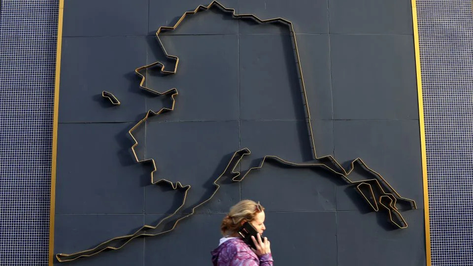 A woman on a cell phone walks by a map of Alaska on July 9, 2022 in Anchorage, Alaska. - Justin Sullivan/Getty Images