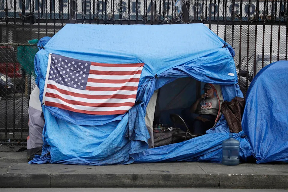 An American flag hangs on the outside of a blue tent on a sidewalk.