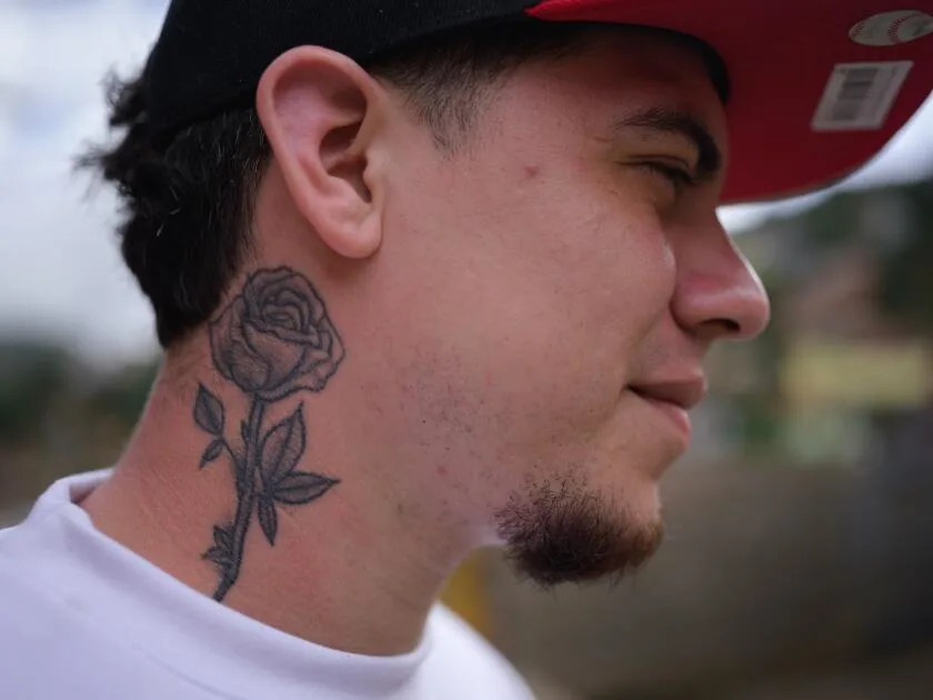 A bearded man in a cap, with a rose tattoo on his neck