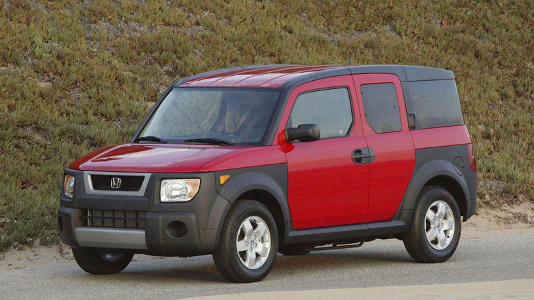 a red honda element parked in front of a grassy hill
